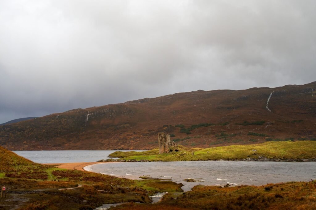 Ruins of Ardvreck Castle beside Loch Assynt beneath cloudy Highland skies.