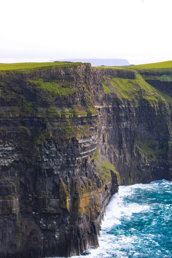 Layered green cliffs descending into the Atlantic Ocean at the Cliffs of Moher in Ireland.