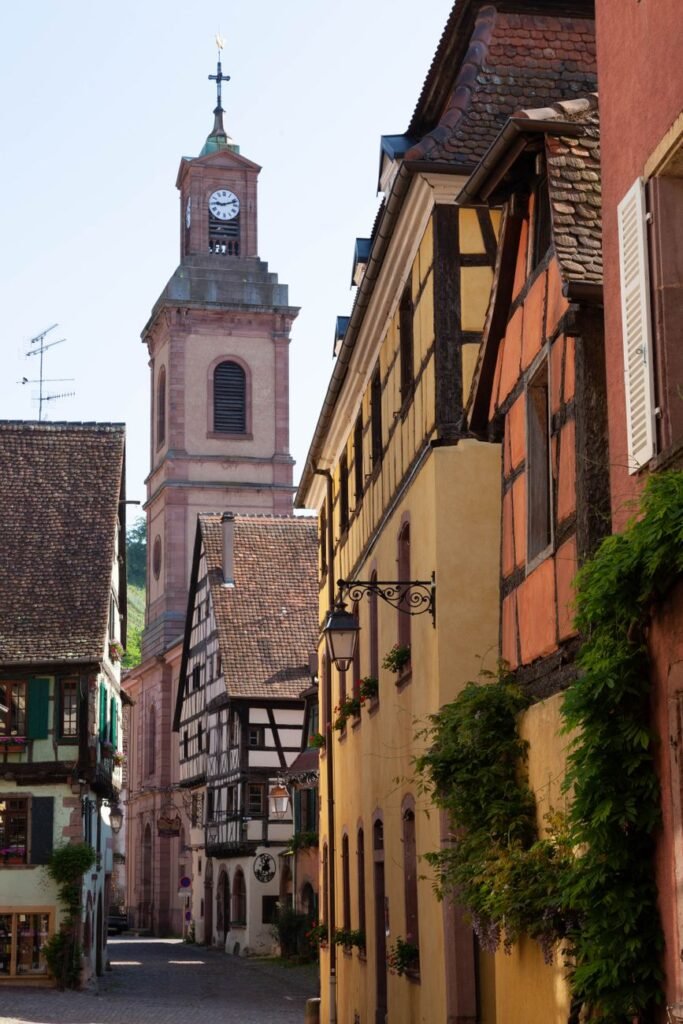 Colourful half-timbered buildings and a clock tower along a medieval street in Riquewihr, France.
