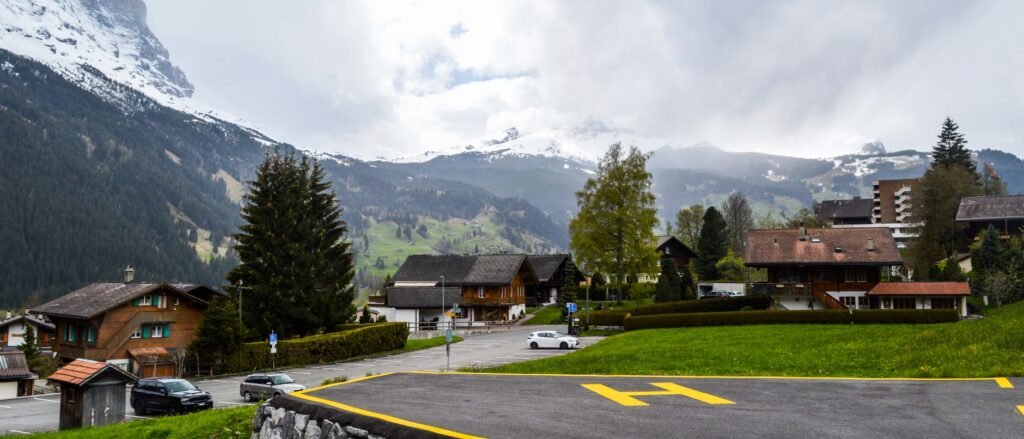 Road and buildings in Grindelwald below green slopes and snow-covered Swiss mountains.
