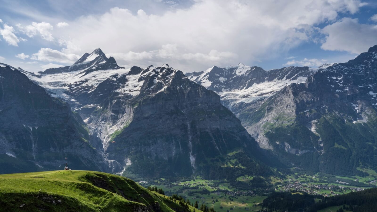 Green Alpine slopes and valley below snow-capped peaks in the Jungfrau region of Switzerland.