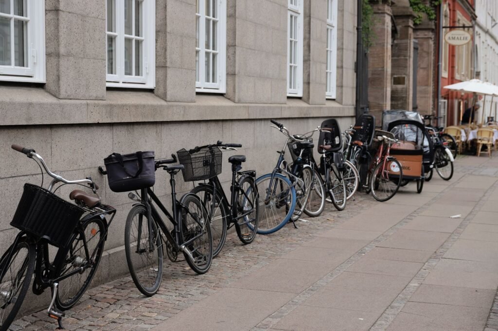 A long row of bicycles parked beside a Copenhagen street and brick buildings.