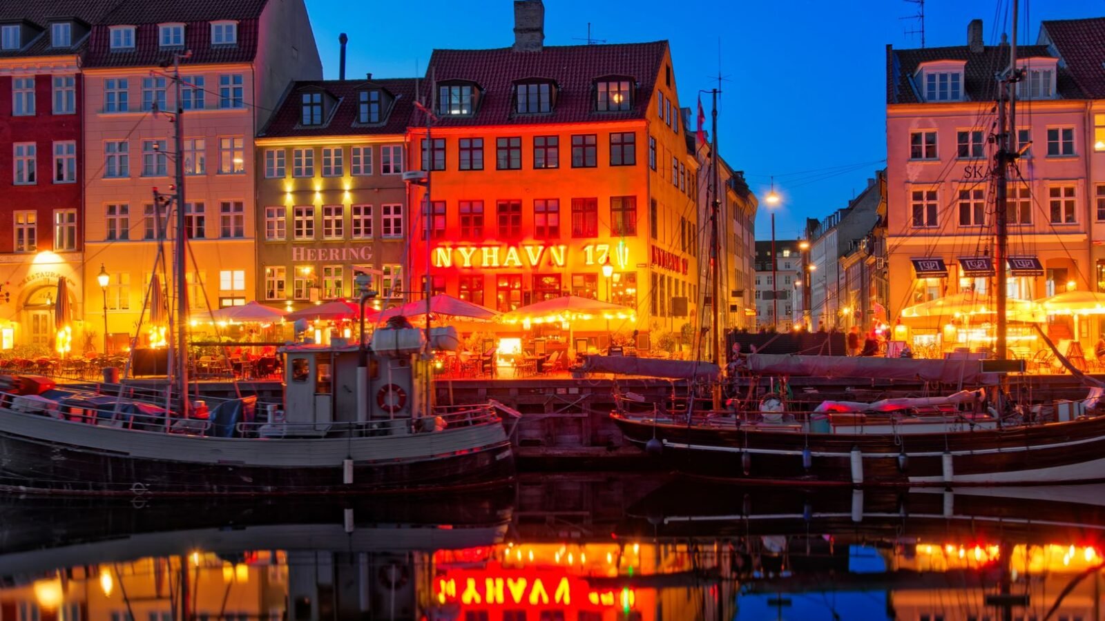 Colourful historic buildings and boats reflected in Nyhavn harbour at dusk in Copenhagen.