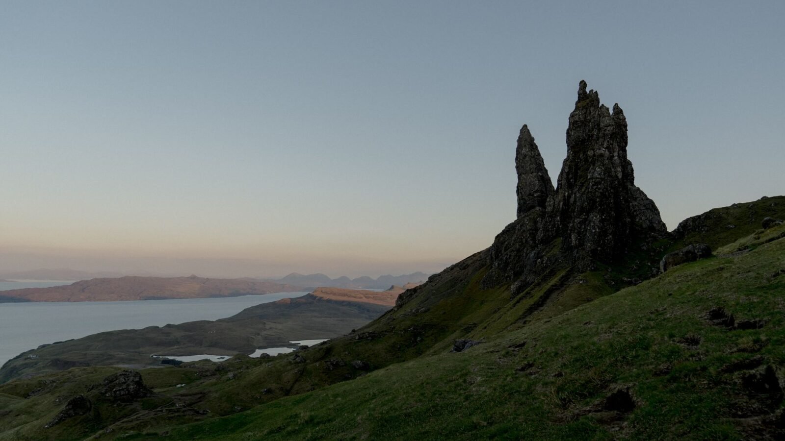 Old Man of Storr rock pinnacles rising above brown-green slopes beneath a pale Scottish sky.