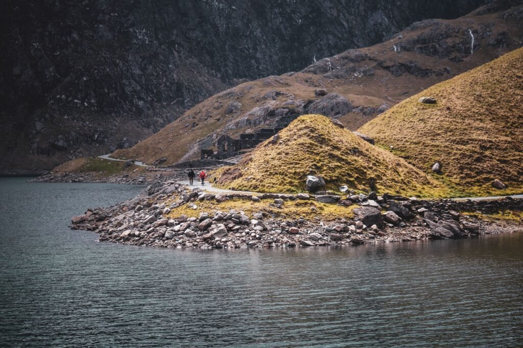 Walkers following a rocky path across a broad mountain landscape in Snowdonia National Park, Wales.
