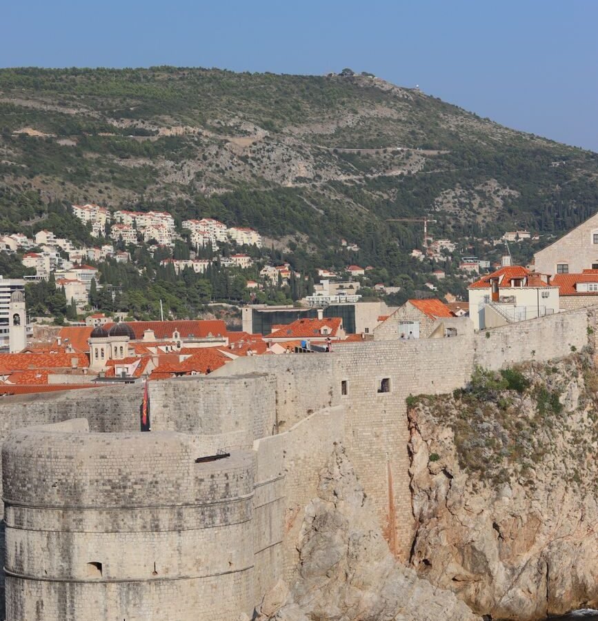 Aerial view of Dubrovnik's stone city walls, red roofs and Fort Bokar beside the Adriatic Sea.