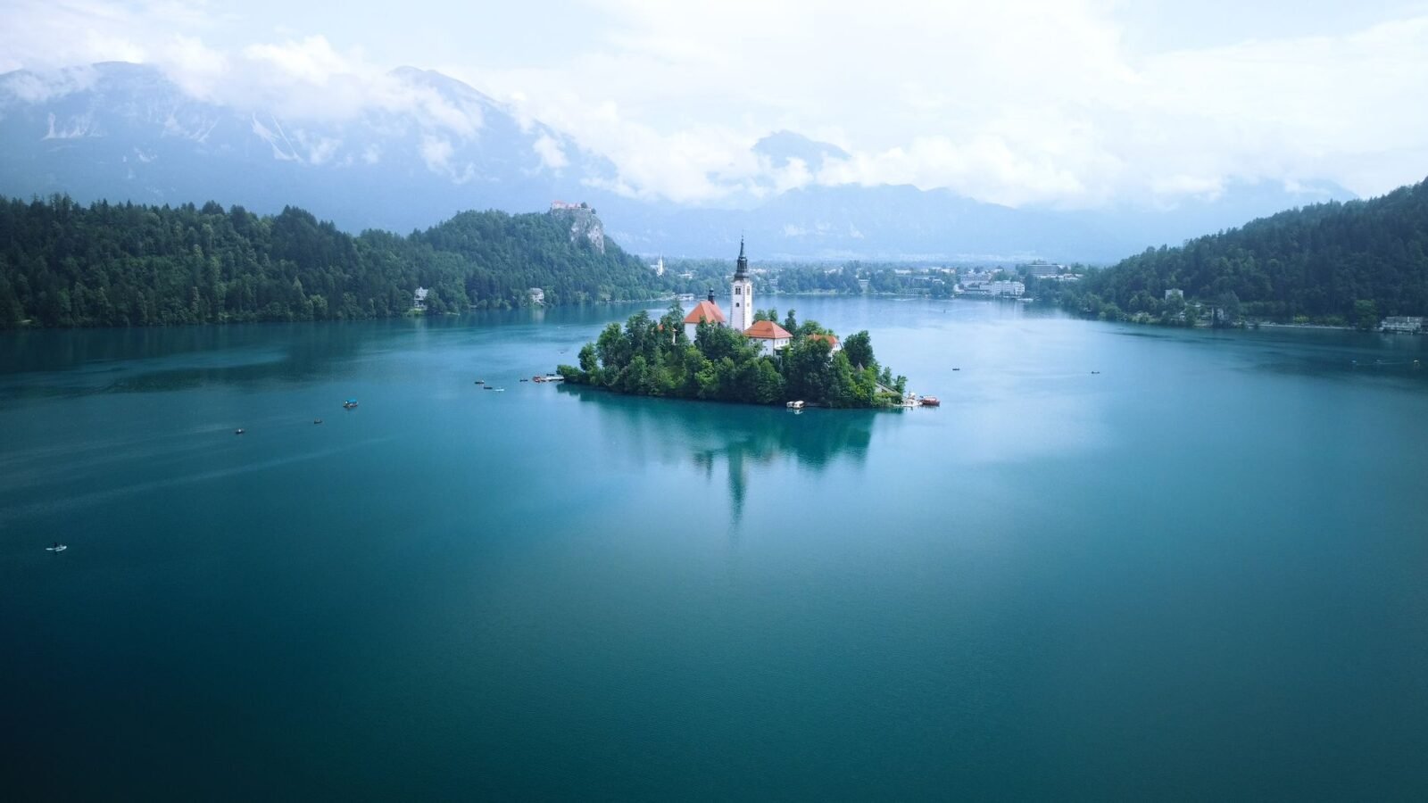 Aerial view of blue Lake Bled with the church-topped island, wooded shore and surrounding Slovenian landscape.
