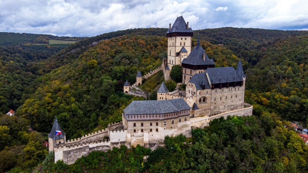 Aerial view of the towers and walled courtyards of Karlstejn Castle surrounded by wooded hills in Czechia.