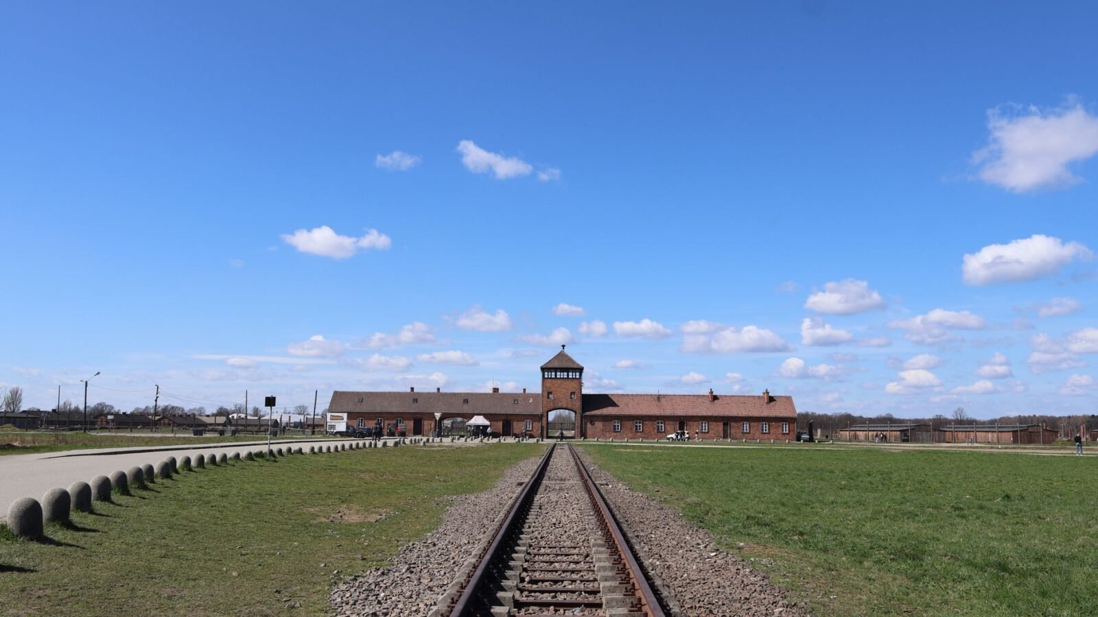 Railway tracks leading toward the brick main entrance building at the Auschwitz II-Birkenau Memorial in Poland.