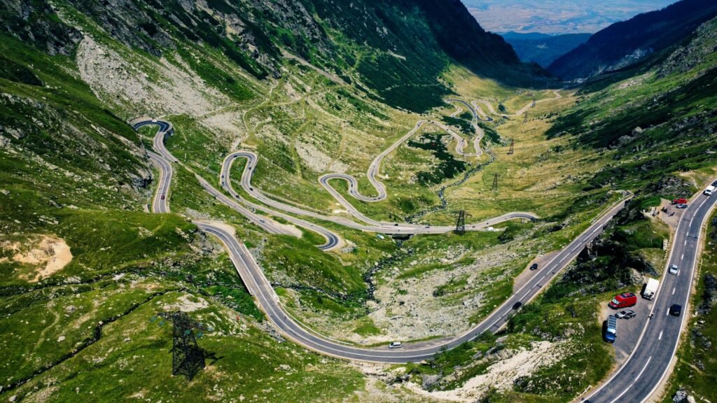 Winding paved sections of the Transfăgărășan road crossing green mountains in Romania.