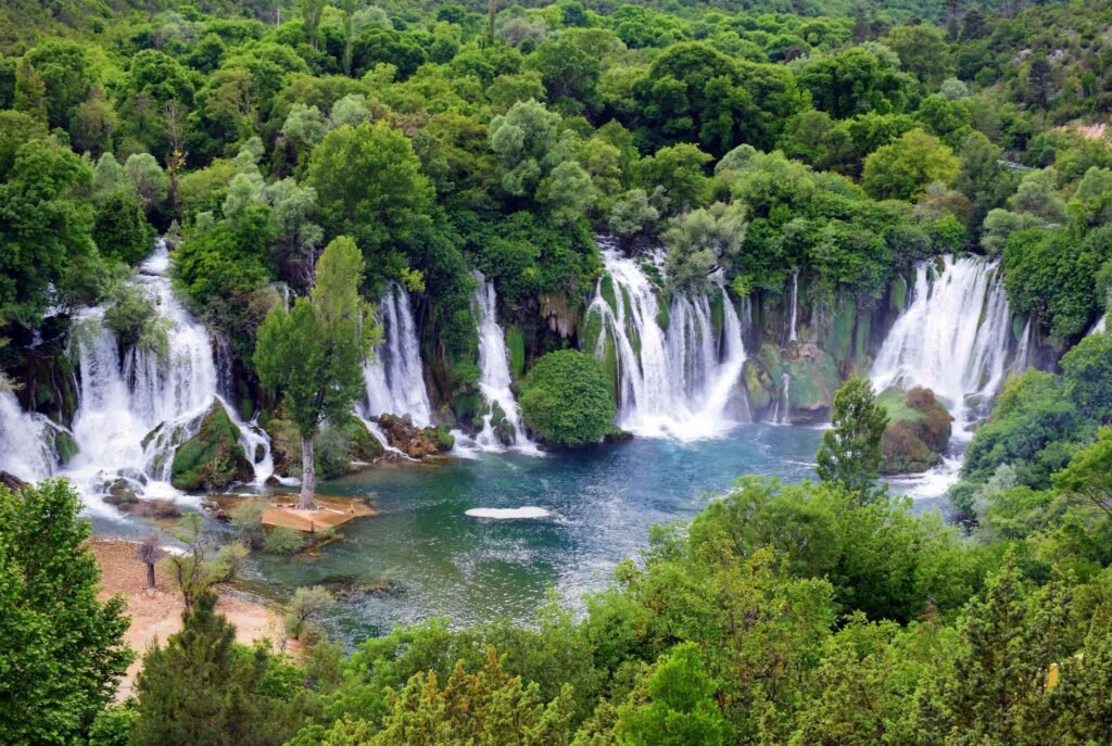 Multiple cascades descending through green vegetation at Kravica Waterfall in Bosnia and Herzegovina.