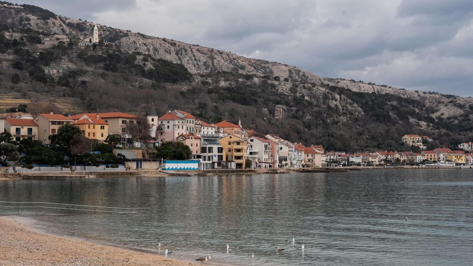 Baška beach and waterfront beneath mountains on Krk island, Croatia.